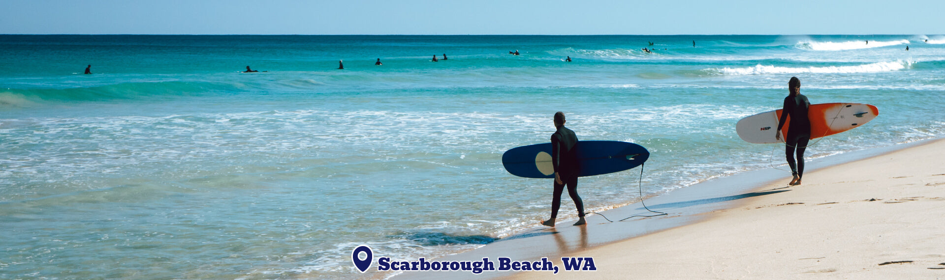 Two surfers with their boards walking along a beach with clear blue water and a banner at the bottom displaying 'Scarborough Beach, WA'.