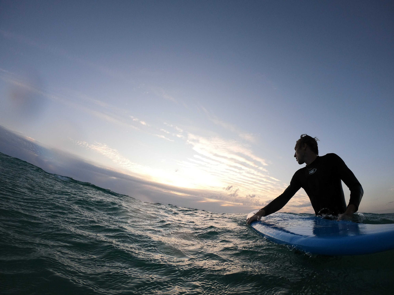 Person surfing at sunset with a dark blue sky and ocean.