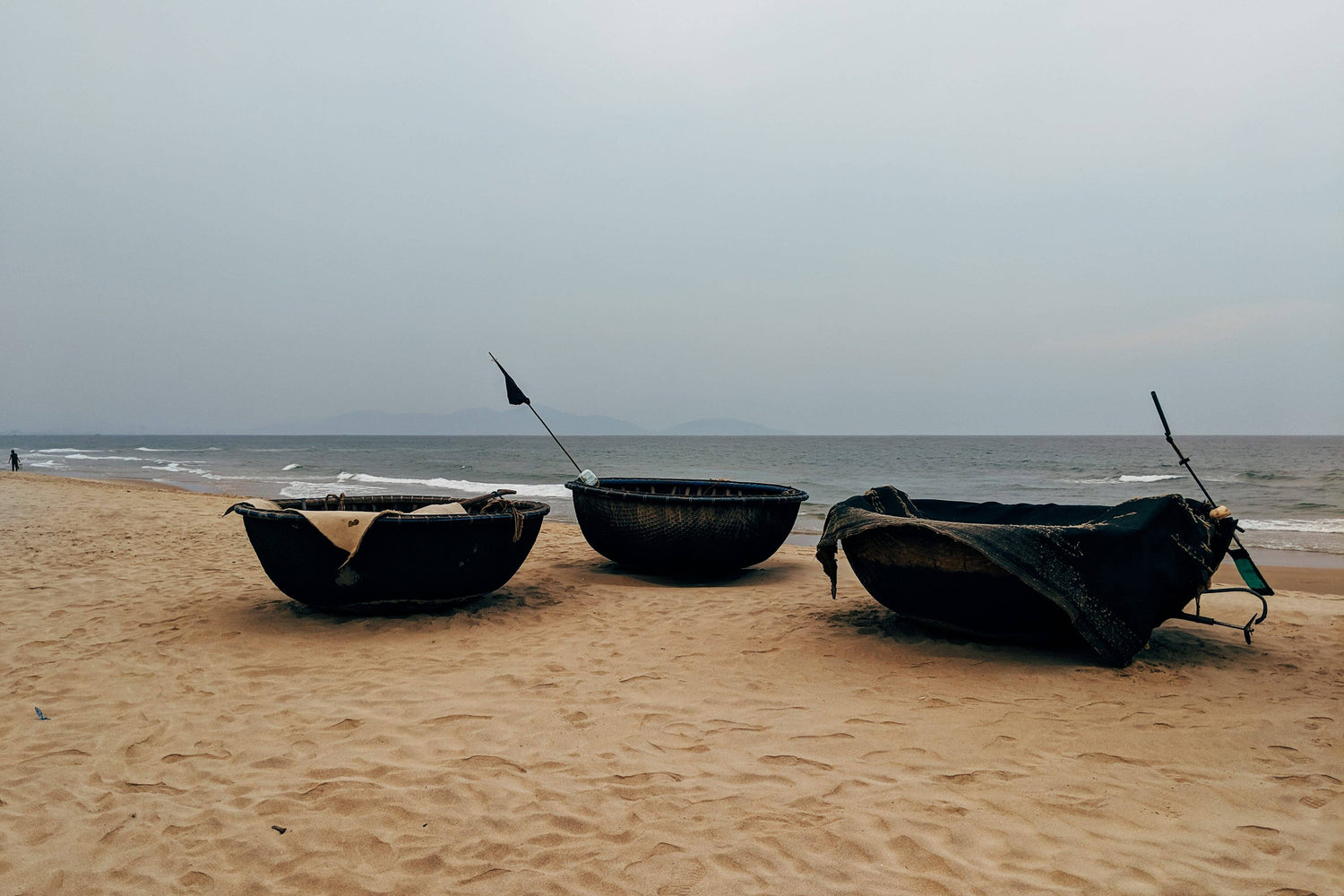 Three traditional boats on a sandy beach with a cloudy sky.