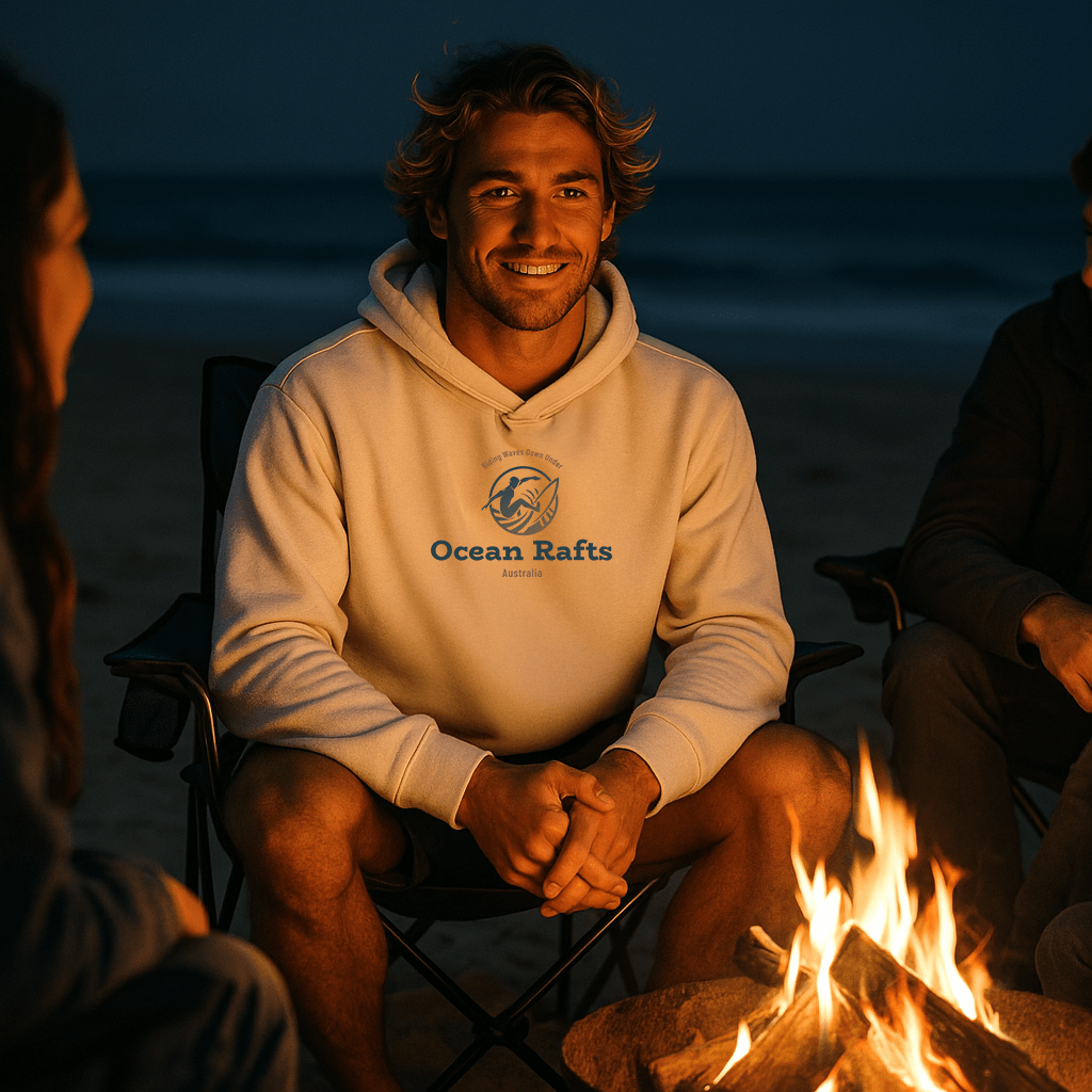 Person wearing an 'Ocean Rafts' hoodie sitting by a campfire on a beach at night.