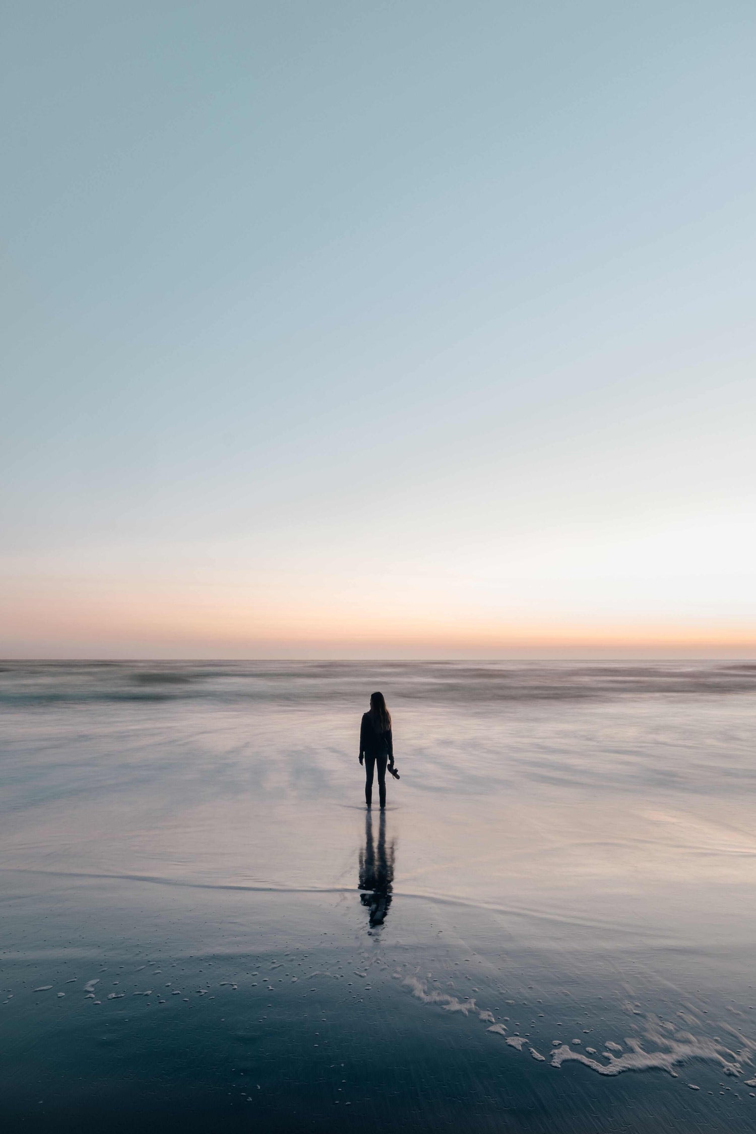 Person standing on a beach at sunset with a minimalistic composition