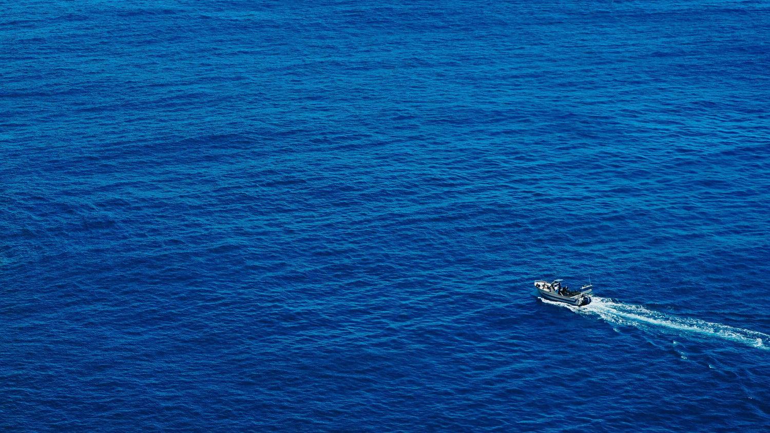 Small boat in the middle of a vast blue ocean